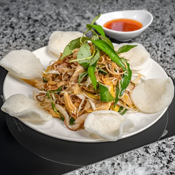 Vietnamese chicken salad with herbs and crispy rice crackers, served with a side of chili sauce.