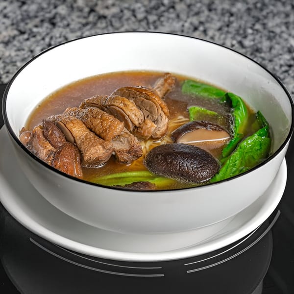 A bowl of Gạo Vietnamese Kitchen's duck noodle soup with mushrooms and green vegetables.