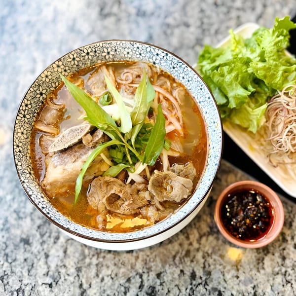 A bowl of Gạo Vietnamese Kitchen's spicy beef noodle soup with herbs, lettuce, and dipping sauce.